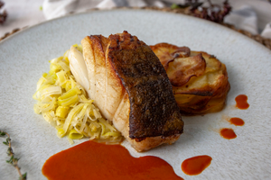 Poached and basted cod served on a bed of buttery leeks and Pomme Anna and a luxurious red pepper and tomato sauce