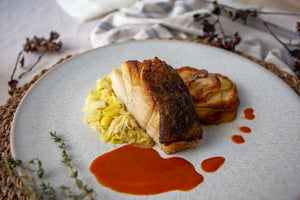 Poached and basted cod served on a bed of buttery leeks and Pomme Anna and a luxurious red pepper and tomato sauce
