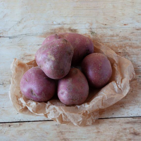 A pile of red potatoes placed on a piece of brown paper, which is laid on a wooden surface.