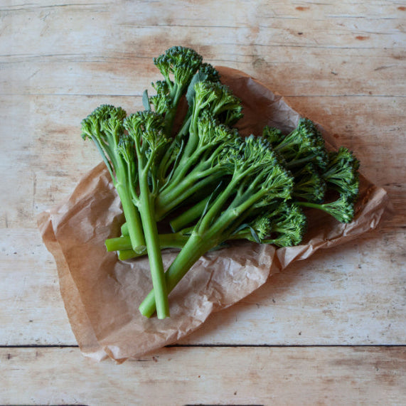 Fresh Tenderstem broccoli on a piece of brown paper, laid on a wooden surface.
