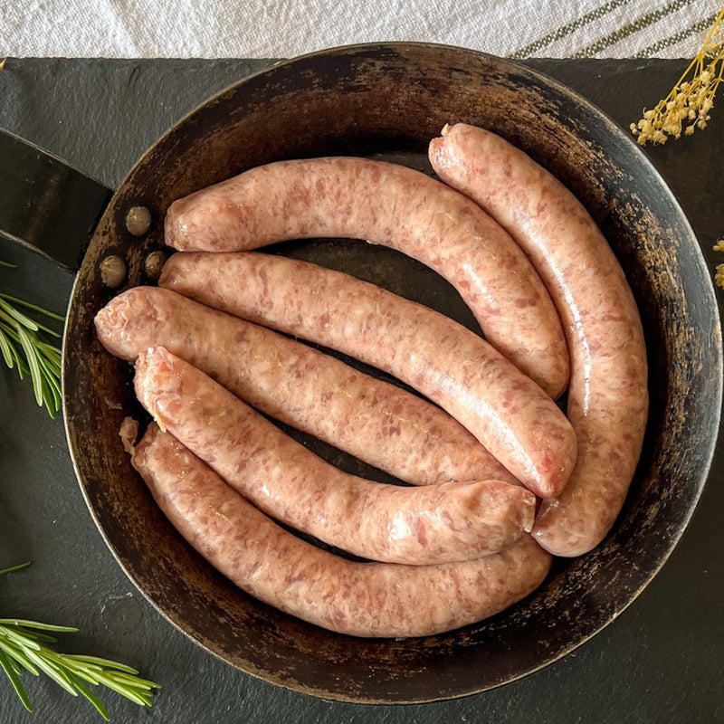 A pan containing uncooked black pudding links, with rosemary sprigs and a yellow flower in the background.