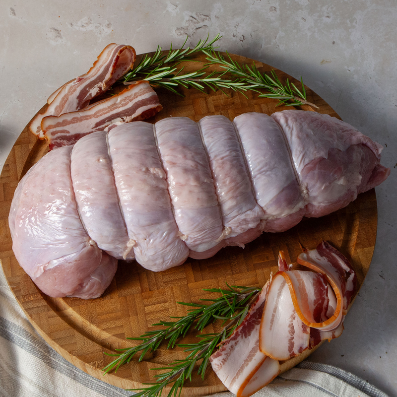A raw lturkey breast on a wooden cutting board, accompanied by rosemary sprigs and slices of lemon.