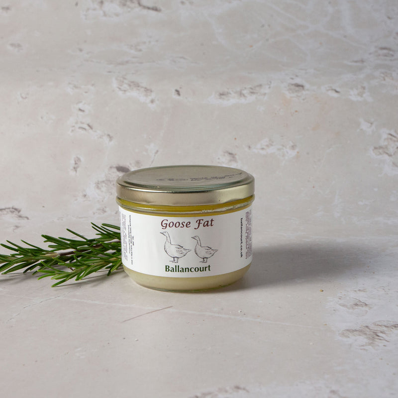 A jar of goose fat on a marble surface with a sprig of gooseberry bush leaves in front of it.