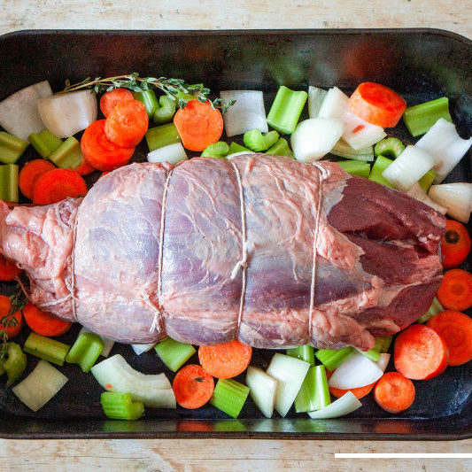 A raw onglet steak lying on top of a bed of vegetables in a roasting tin, ready for cooking.