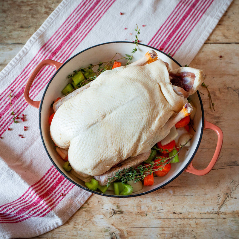 A whole duck with vegetables is placed in a roasting pan, which is set on a kitchen towel with red stripes.